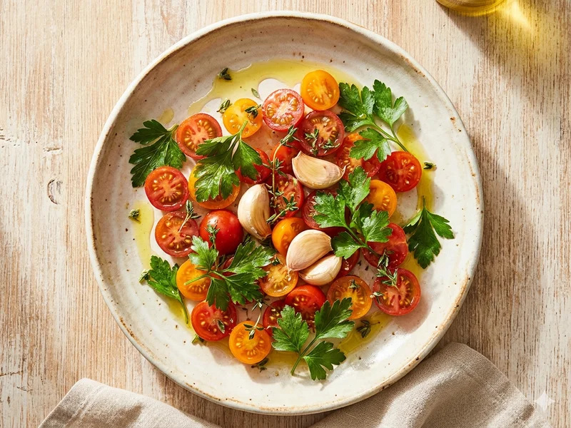 Vue de dessus d&rsquo;une assiette de cuisine méditerranéenne avec huile d&rsquo;olive, tomates, herbes fraîches et plusieurs gousses d&rsquo;ail, ambiance lumineuse et chaleureuse, style food éditorial